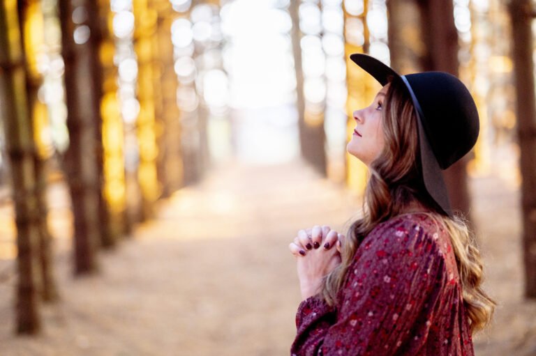A selective focus shot of a beautiful young lady praying in a forest